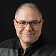 Smiling older man wearing glasses, professional headshot against a neutral background.