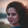 Smiling woman with dark hair looking to the side, portrait with soft natural lighting.